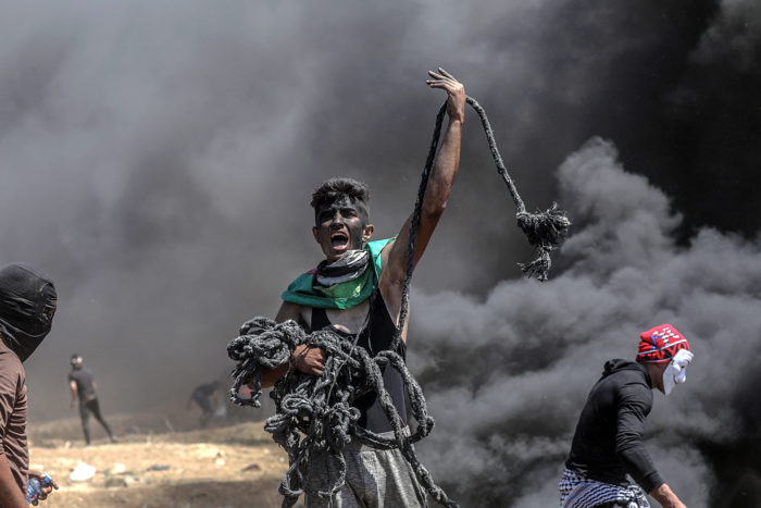 Gáza, 2018. május 14. Palesztin tüntető kötéllel a kezében égő gumiabroncsok füstjében az enklávét Izraeltől elválasztó kerítés mellett, Gáza városától keletre 2018. május 14-én. A nap folyamán több tízezer palesztin tiltakozott az amerikai nagykövetség Tel-Avivből Jeruzsálembe való átköltöztetése miatt. A palesztin egészségügyi hatóság összesítése szerint a Gázai övezet határán zajló összecsapásokban 52 palesztin vesztette életét, s több mint kétezren megsérültek. Az izraeli katonák könnygázzal és éles lőszerrel válaszoltak a palesztinok kerítést megközelítésére tett kísérleteire.(MTI/EPA/Mohammed Szaber)