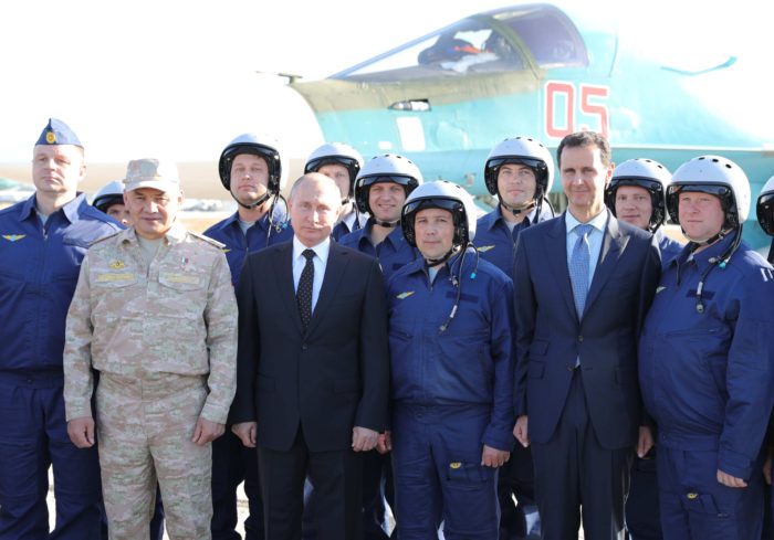 Hmejmími légitámaszpont, 2017. december 11. Vlagyimir Putyin orosz elnök (b4), Szergej Sojgu orosz védelmi miniszter (b2) és Bassár el-Aszad szíriai elnök (j3) pilótákkal fényképezkedik a szíriai Hmejmímnél működő orosz légitámaszponton 2017. december 11-én. Putyin a bázison tett villámlátogatásán elrendelte az orosz csapatok Szíriából történő visszavonásának megkezdését. (MTI/AP/Szputnyik/Kreml pool/Mihail Klimentyev)
